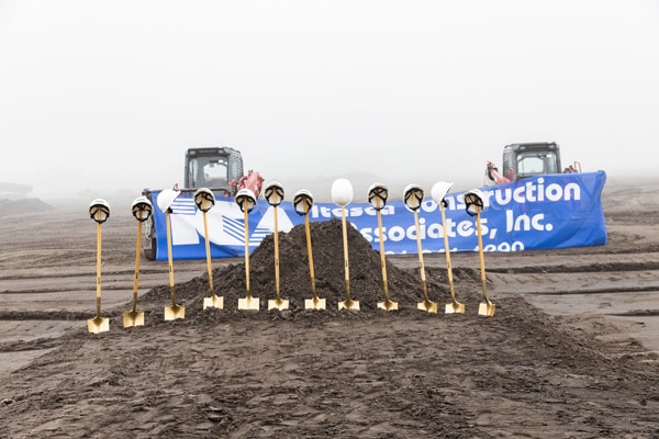 A bunch of gold shovels holding white construction hats perched in front of two bulldozers holding a sign for a construction company.