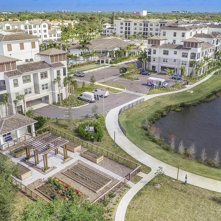 An aerial side view of the Arcadia Gardens building apartment/living complex next to a pond and community garden.